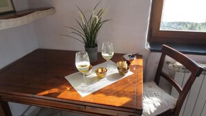 Een houten tafel met twee glazen witte wijn, een kleine plant in pot en een schaal met lekkernijen.