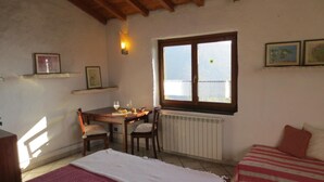 Een gezellige kamer met een houten tafel, twee stoelen, een bed met een gestreept dekbed en een radiator, plus een raam met uitzicht.
