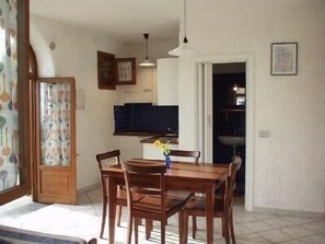 A dining area with a wooden table and chairs, a hanging light fixture, and a kitchen in the background. - Rustico Vinsa, monolocale con giardino panoramico edificio separato (Chiusanico)