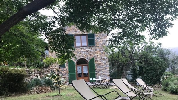 Een gebouw van steen met een groene deur en luiken, omringd door een gazon met lounge stoelen.