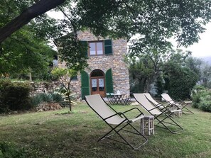 A stone building with a green door and shutters, surrounded by a grassy area with lounge chairs. - Rustico Vinsa, monolocale con giardino panoramico edificio separato (Chiusanico)