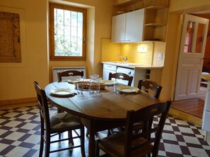 A dining area with a checkered floor, a wooden table, and chairs. There is a window with a view of greenery outside.