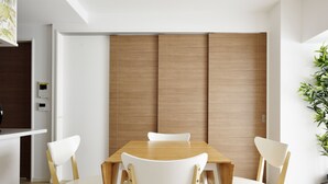 Un comedor moderno con una mesa de madera y sillas blancas, una puerta de madera corredera y una planta en maceta a la derecha.