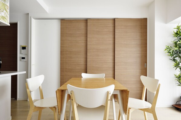Un comedor moderno con una mesa de madera y sillas blancas, una puerta de madera corredera y una planta en maceta a la derecha.