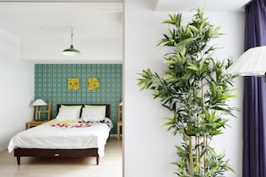 Quarto com cama, parede revestida de azulejos verdes, duas luminárias fixadas na parede e um vaso de planta.