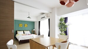 Una habitación de hotel moderna con una cama, una mesa de comedor, sillas, una planta en maceta y un ventanal grande.