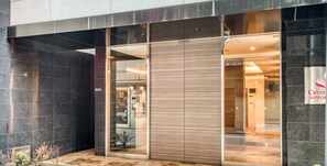 Una entrada de edificio moderno con puerta de vidrio, cartel de 'Crystal Nippon' y piso de baldosas.
