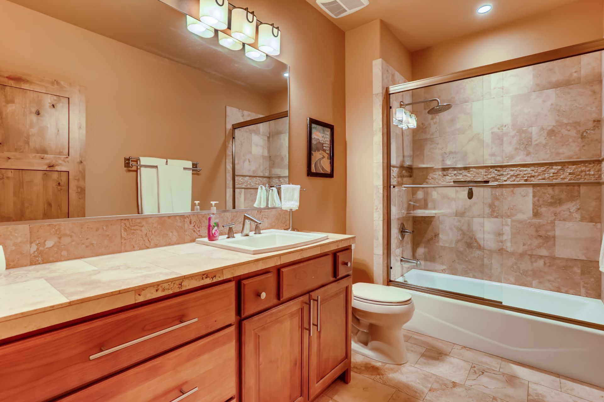 A modern bathroom with a wooden vanity, a large mirror, a shower with a glass door, and a toilet.