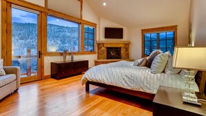 Une chambre à coucher avec un grand lit, une cheminée et une vue sur un paysage enneigé, visible à travers de grandes fenêtres.