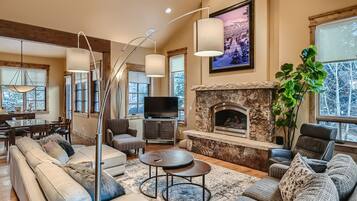 A spacious living room with a stone fireplace, a large sofa, a television, and a dining area with a wooden table and chairs.