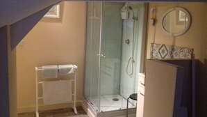 Un petit espace douche fermé, doté d’une porte en verre, d’un porte-serviettes blanc et d’un miroir mural.