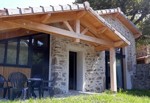 A stone building with a wooden roof, a covered patio with chairs, and a stone wall. - Bright cottage with terrace and pets allowed (Doizieux)