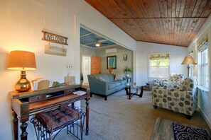 A living room with a sofa, armchairs, a coffee table, and a lamp. There is a wooden ceiling and a window with curtains.