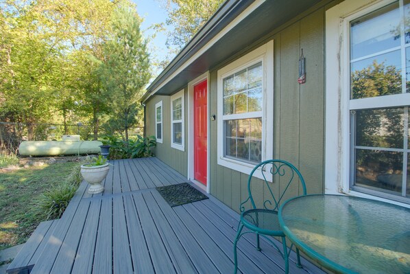 A wooden deck with a glass table and chairs, a red door, and a window with a view of trees.