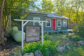 A cottage with a wooden sign, a red door, and a garden with rocks and plants.