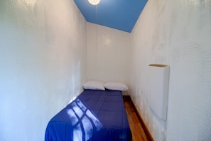 A small, narrow room with a single bed, white walls, and a blue ceiling.