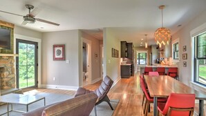 A spacious dining area with a long wooden table and red chairs, a stone fireplace, and a view of the outdoors. - Charming Farmhouse Hot Tub Three Acres (Candler)
