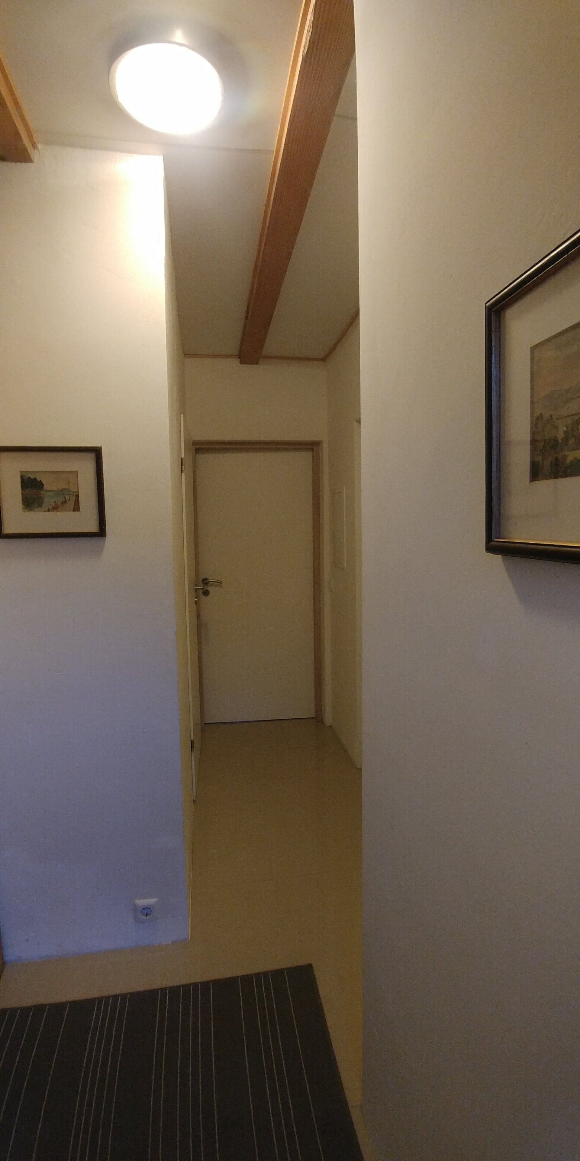 A narrow hallway with a door at the end, a framed picture on the wall, and a ceiling light.