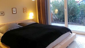 A bedroom with a wooden bed frame, a large window with curtains, and a hanging light fixture. - Pension on the Elbe bridge - Apartment New Venice (Berlin)