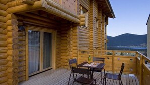 Eine Holzblockhütte mit einer Holzdiele, einem Tisch mit Stühlen und Blick auf die Berge.