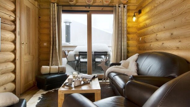 Ein Holzblockhaus-Interieur mit einem Ledersofa, einem Holztisch und einer Essecke mit Tisch und Stühlen.