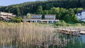 A lakeside property with modern buildings, a dock, and a forested hill in the background.