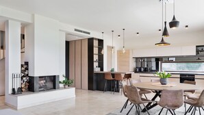 A modern kitchen with a dining area, featuring a central island, pendant lighting, and a view of the outdoors.