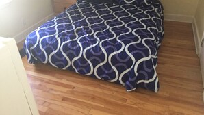 Una camera da letto con una coperta a motivi, pavimento in legno, un comodino e una lampada.