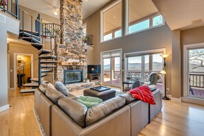 A spacious living room with a stone fireplace, a large leather sofa, and a staircase leading to an upper level. - Sky Valley Home w/ Mtn View, 5 Mi to Rabun Bald! (Sky Valley)