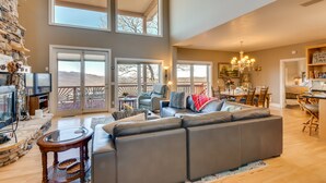 A spacious living area with a large sectional sofa, a stone fireplace, and a dining area with a chandelier. - Sky Valley Home w/ Mtn View, 5 Mi to Rabun Bald! (Sky Valley)