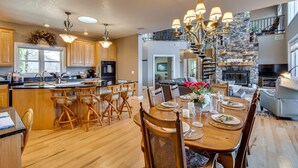 A spacious kitchen with wooden cabinets, a large island with bar stools, and a dining area with a wooden table set for four. - Sky Valley Home w/ Mtn View, 5 Mi to Rabun Bald! (Sky Valley)