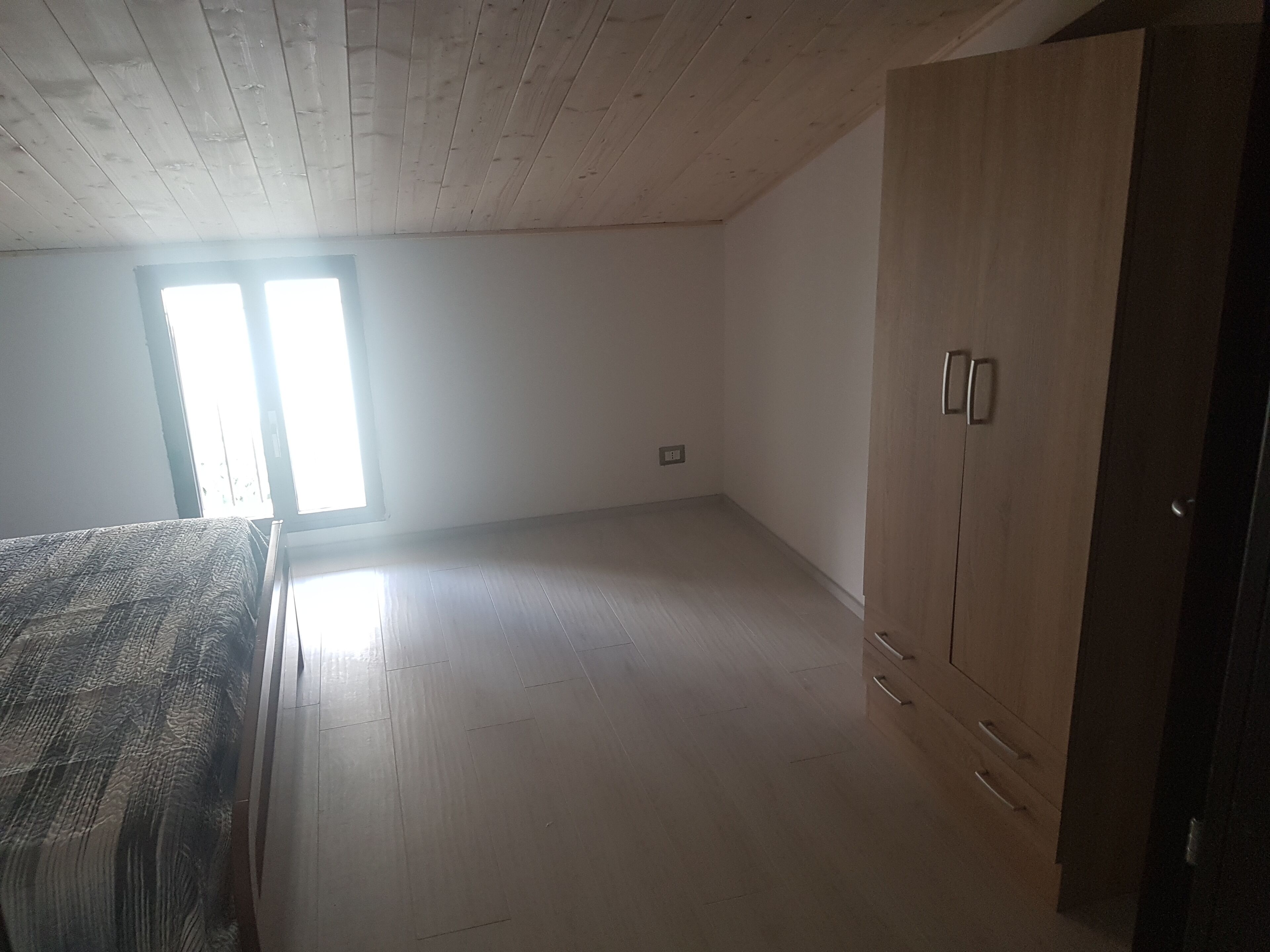 Um quarto com piso de madeira, guarda-roupa e janela com iluminação natural.