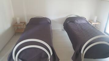 Two single beds with white metal frames and dark covers in a room with white walls and a wooden floor.