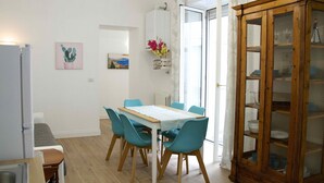 A dining area with a wooden table and teal chairs, a cabinet with glass doors, and a wall-mounted flower arrangement. - Fabiana house, apartment in the historic center for short or long periods (Napoli)