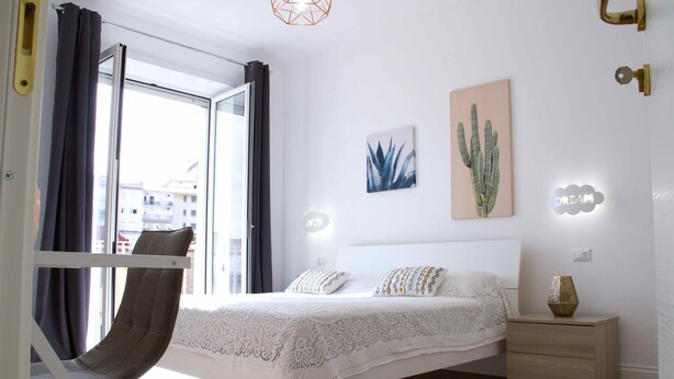 A bedroom with a bed, nightstand, chair, and artwork on the wall. - Fabiana house, apartment in the historic center for short or long periods (Napoli)