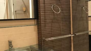 A modern bathroom with a glass sink, a large mirror, and a walk-in shower with a glass door.
