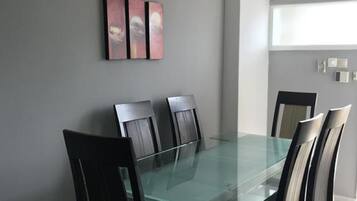 A dining area with a glass table and dark chairs, a gray wall, and a window with an air conditioner.