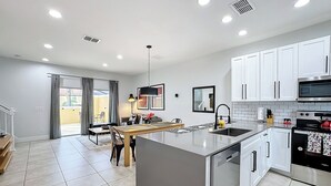 A modern kitchen with white cabinets, a stainless steel dishwasher, and a large island with a sink. - A Dream Villa next to Disney. (Kissimmee)