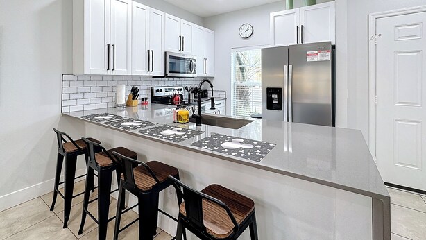 A modern kitchen with white cabinets, a stainless steel refrigerator, a microwave, and a large island with bar stools. - A Dream Villa next to Disney. (Kissimmee)