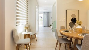 Uma sala de jantar moderna com uma mesa de madeira redonda, cadeiras estofadas cinzentas e um vaso com flores secas.