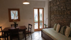 A room with a dining table, chairs, a sofa, a potted plant, and a stone wall.