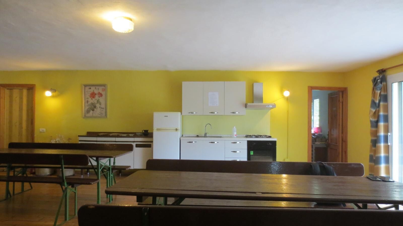 Une cuisine compacte avec des meubles blancs, un évier et une cuisinière. On peut voir des bancs en bois et une table au premier plan.