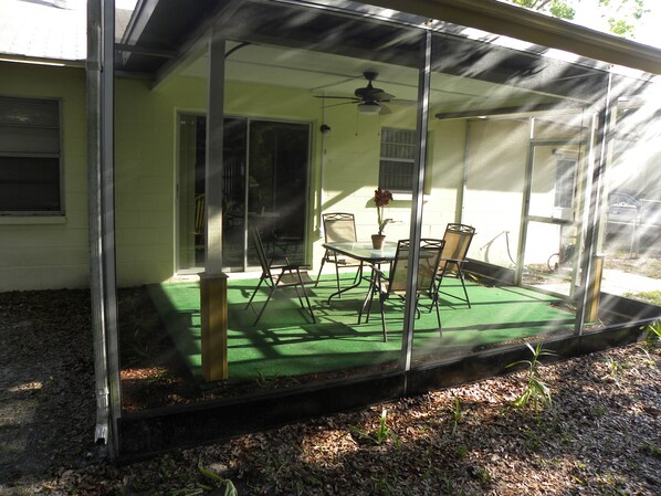 A covered patio with a table and chairs, a ceiling fan, and a potted plant.