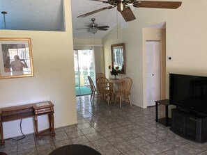 A living room with a ceiling fan, a TV, a dining area with chairs, and a small table.