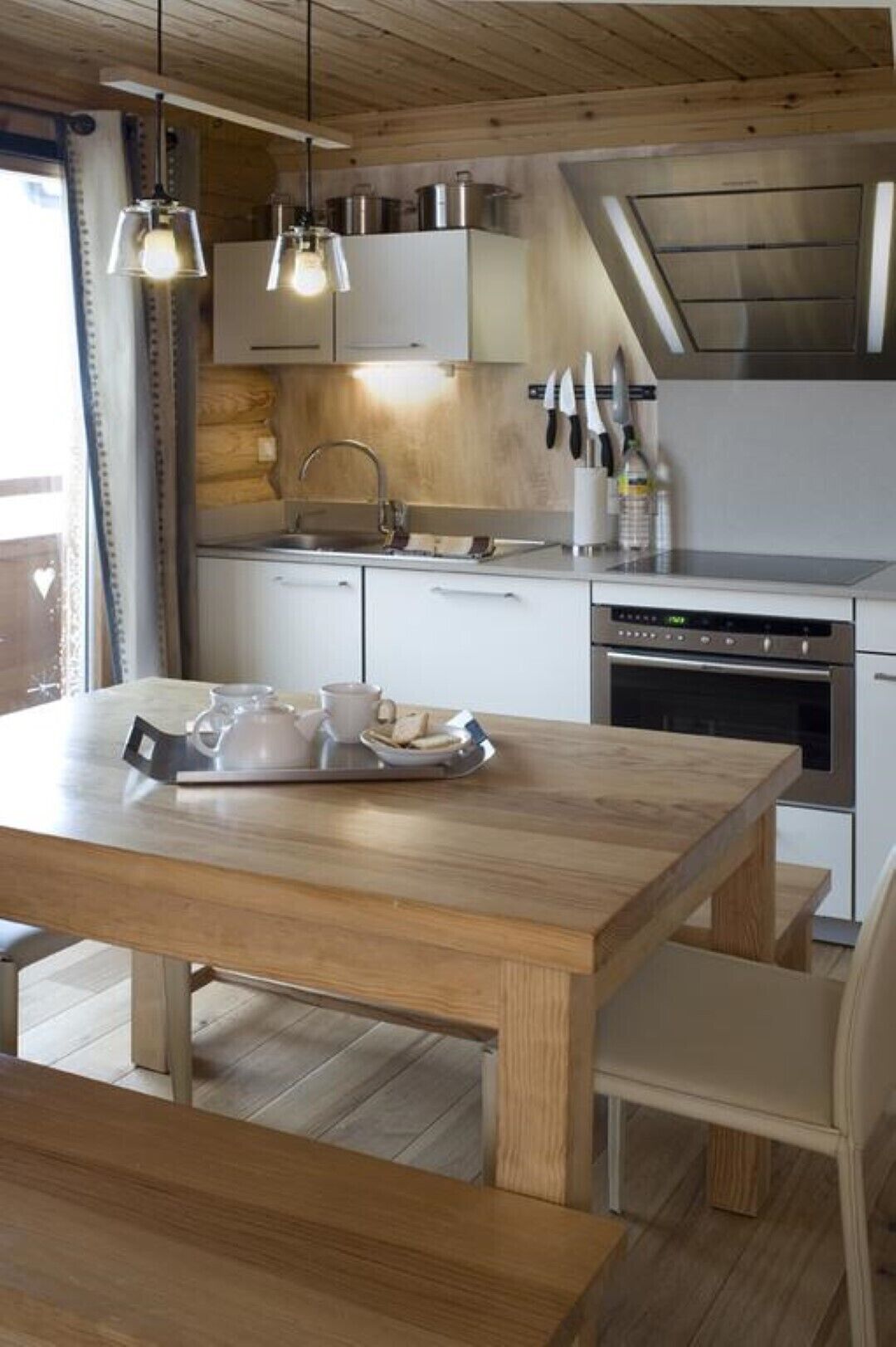 A modern kitchen with wooden cabinetry, a built-in oven, and a dining table set with cups and a tray.