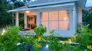 Ein modernes Haus mit überdachter Veranda, einem sichtbaren Wohnzimmer mit Sofa und einem großen Fenster mit Vorhängen.