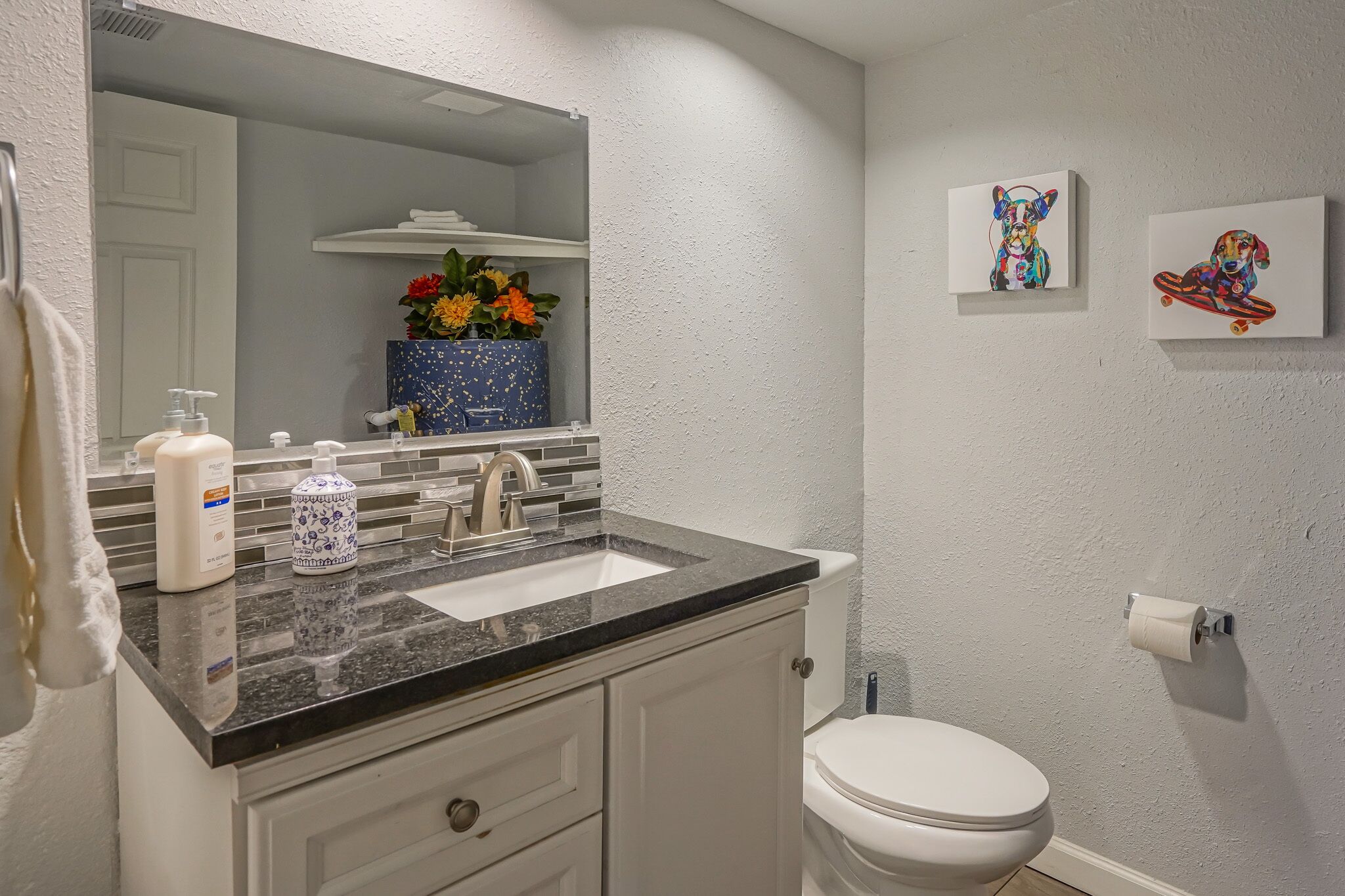 A bathroom with a white toilet, a sink with a marble countertop, a mirror, and two framed artworks on the wall.