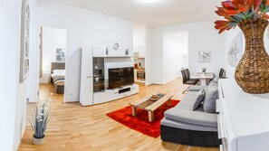 A modern living room with a flat-screen TV, a grey sofa, a red rug, and a wooden coffee table.