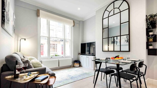 A modern living room with a sofa, a dining table with chairs, a TV, and a large window. - Comfy Bayswater Apartment (London)