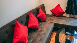 Ein modernes Wohnzimmer mit einer braunen Ledersofa, roten Kissen, einem Glastisch und einem Stadtbild an der Wand.